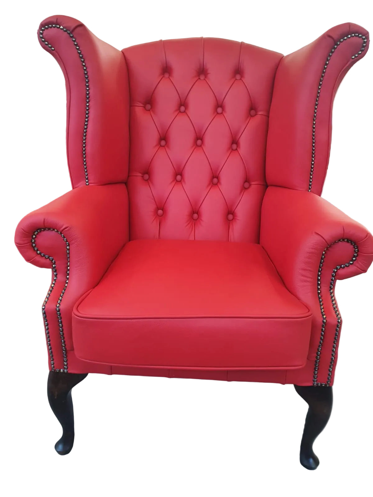 Red upholstered armchair with tufted backrest and nailhead trim on a concrete floor.